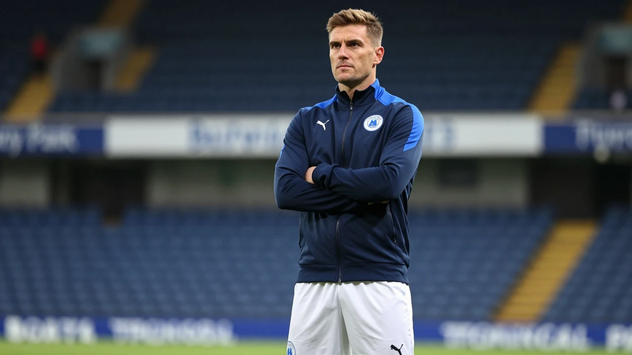 A young, muscular Oldham Athletic coach in a navy blue tracksuit and white shorts stands confidently with arms crossed...