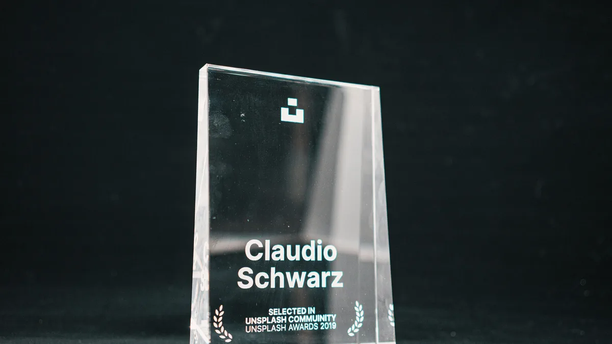 Film: A clear glass or crystal award with the name "Claudio Schwarz" engraved on it, placed on a dark surface.