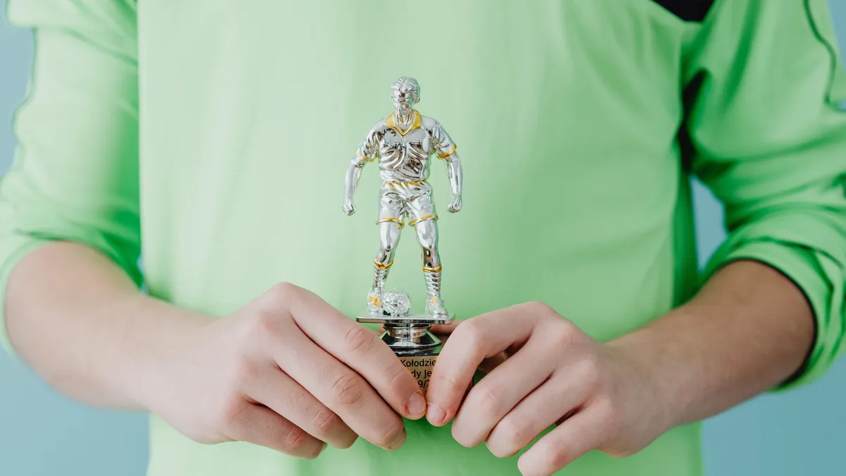 Film: A person holding a silver soccer trophy against a blue background.
