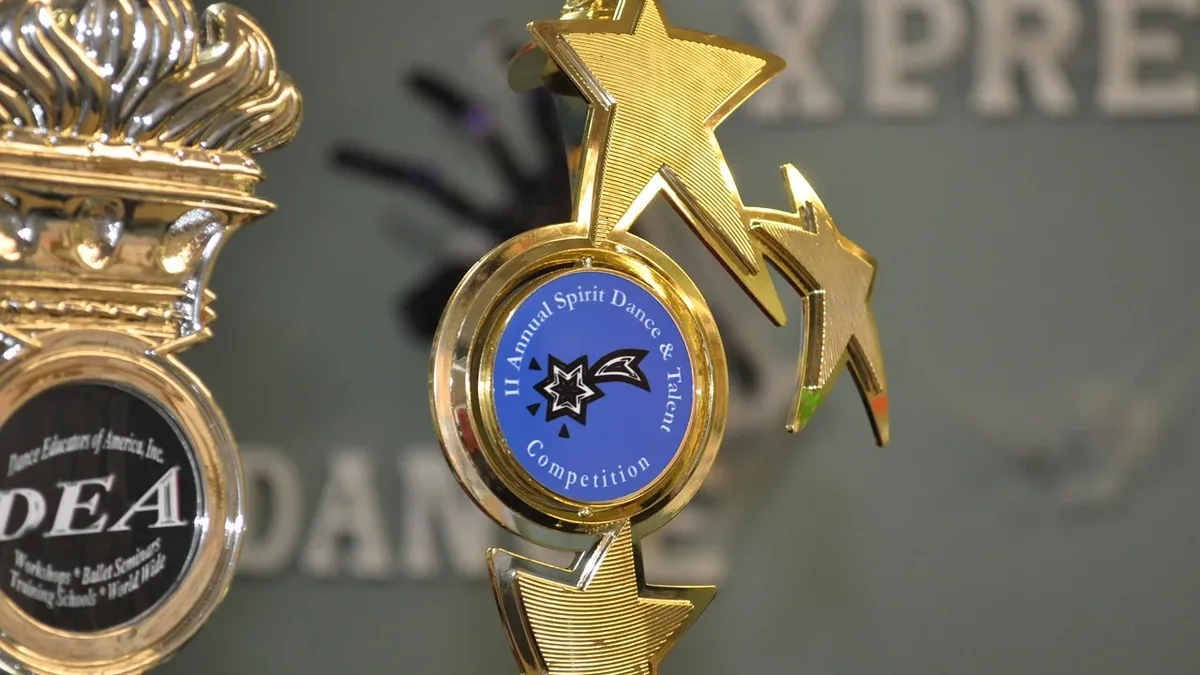 Film: A close-up of a gold trophy with a blue circular logo featuring a star and the words "Annual Sports Dance & Talent