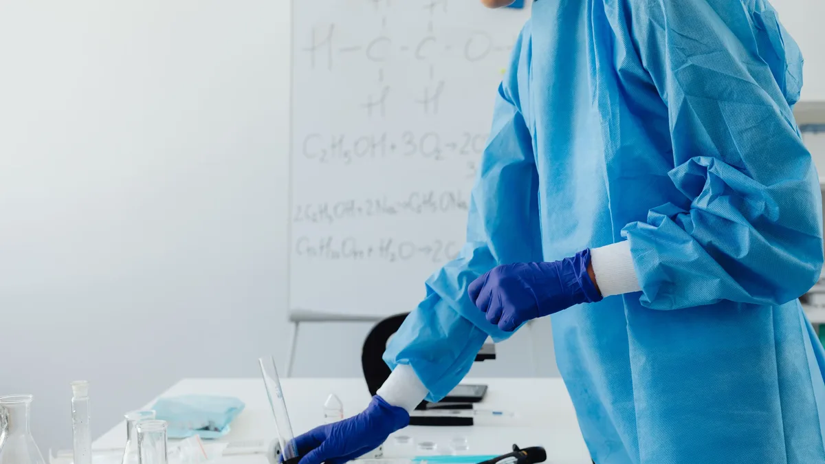 Evidence: Scientist in protective clothing working in lab with chemical formulas on whiteboard.