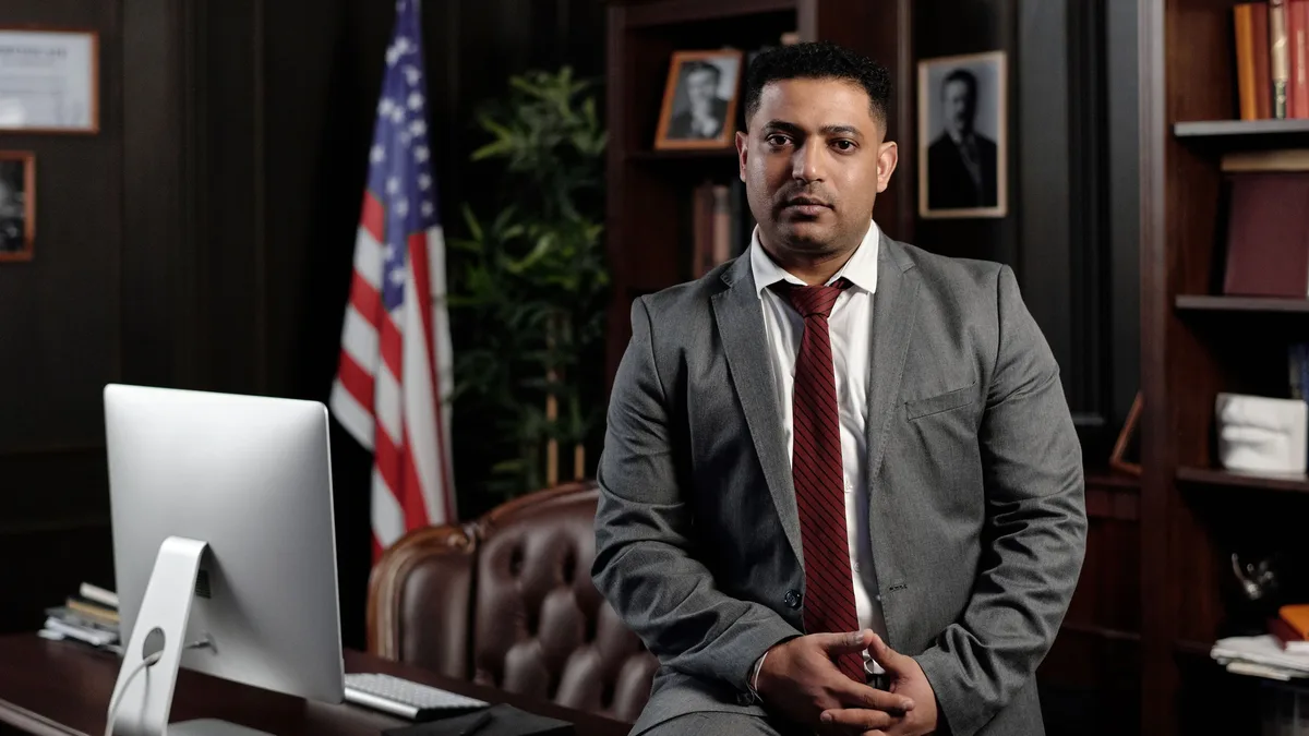 Elections: A professional businessman in a suit sitting in an office setting, with the American flag in the background.