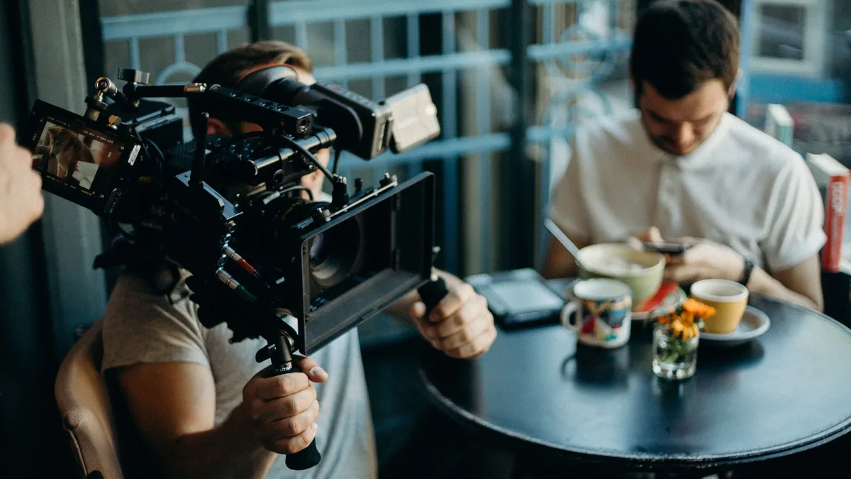 Films: Cameraman filming a scene in a cozy cafe setting, capturing the atmosphere.