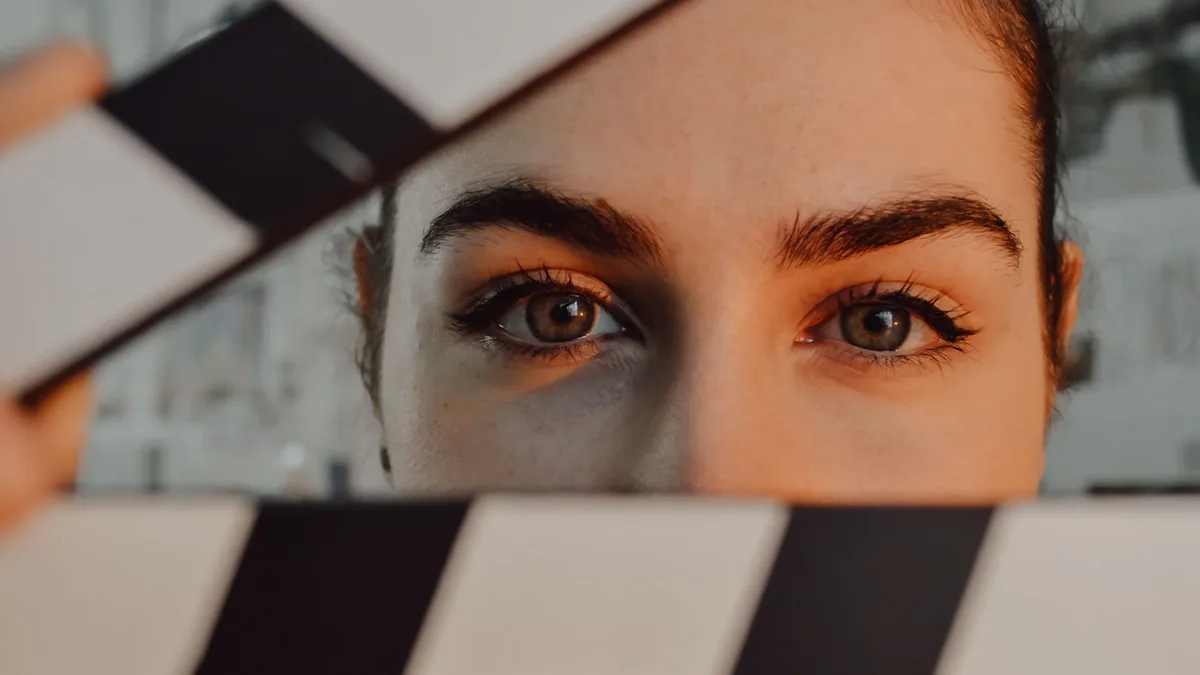 Streaming: Intriguing close-up of a person's eyes behind a movie clapperboard, symbolizing filmmaking artistry.