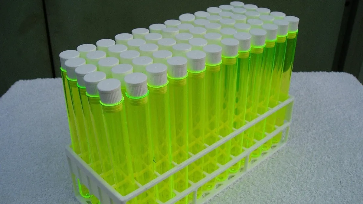 Titles: A stack of 50 yellow test tubes with white caps, arranged in a plastic rack on a white surface.
