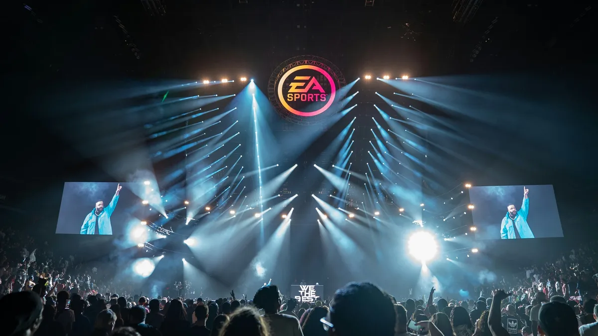 A concert stage with a crowd of people in front of it, featuring a large screen displaying a man in a blue shirt and a logo