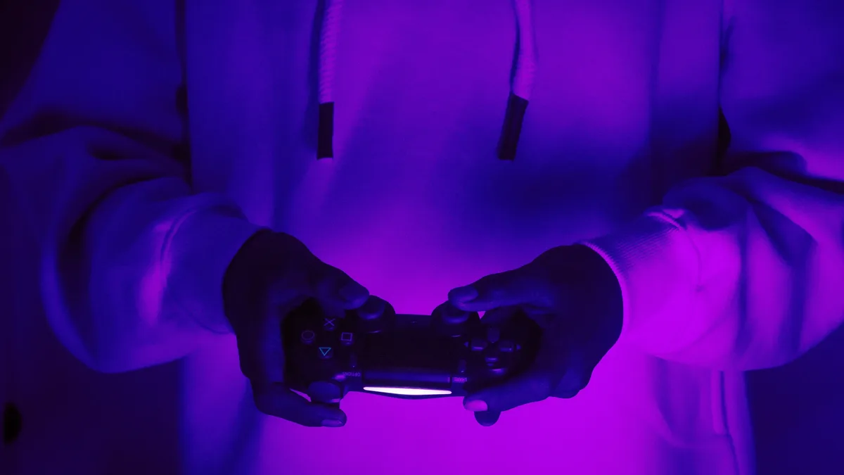 Focused gamer in hoodie holding a PlayStation controller under purple light, creating a vibrant gaming vibe. Esports close up