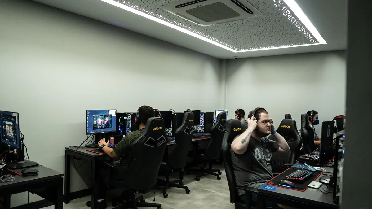 A group of people are seated at computer desks in a room with white walls and a white ceiling, engaged in an activity that