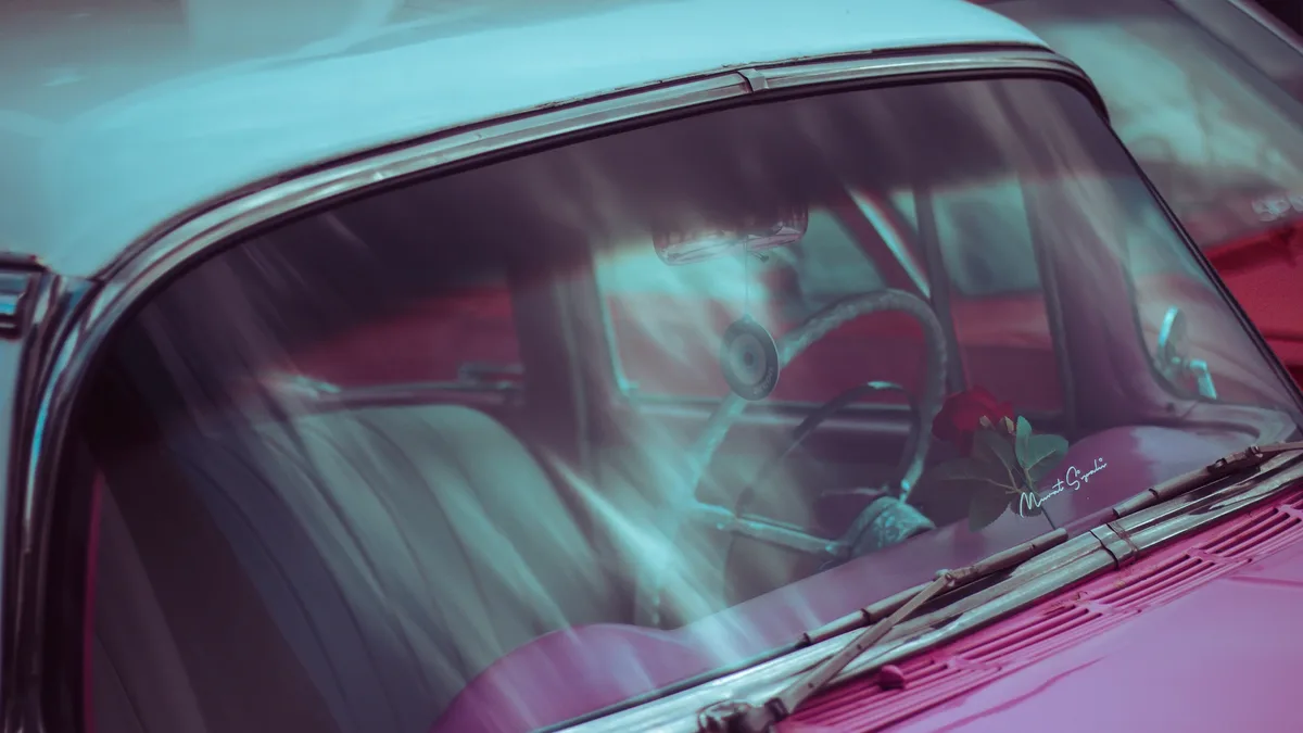 Eras: The front windshield and dashboard of a vintage car, with a steering wheel and a pink interior.