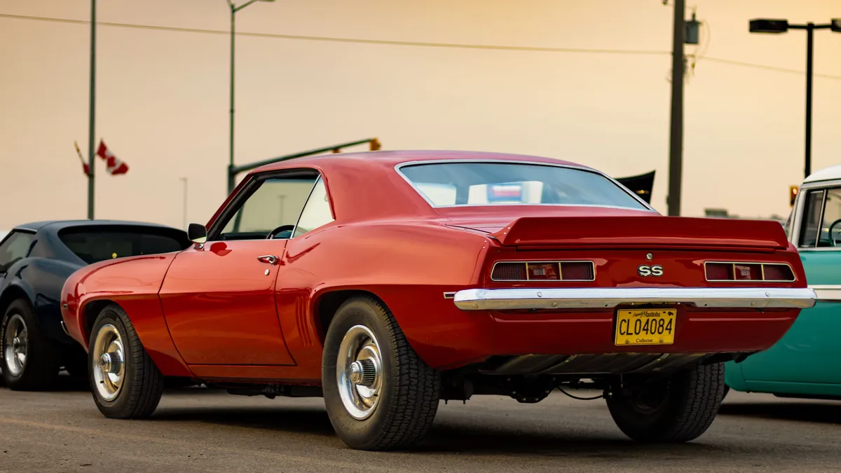 A red Chevrolet Camaro SS parked in a lot with other cars, featuring a yellow license plate with the registration number