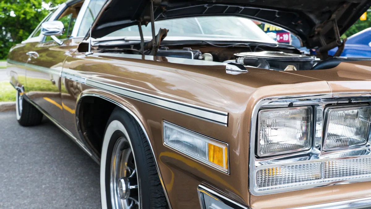 Auctions: Close-up of a vintage brown car with an open hood showcasing its engine in an outdoor parking lot.