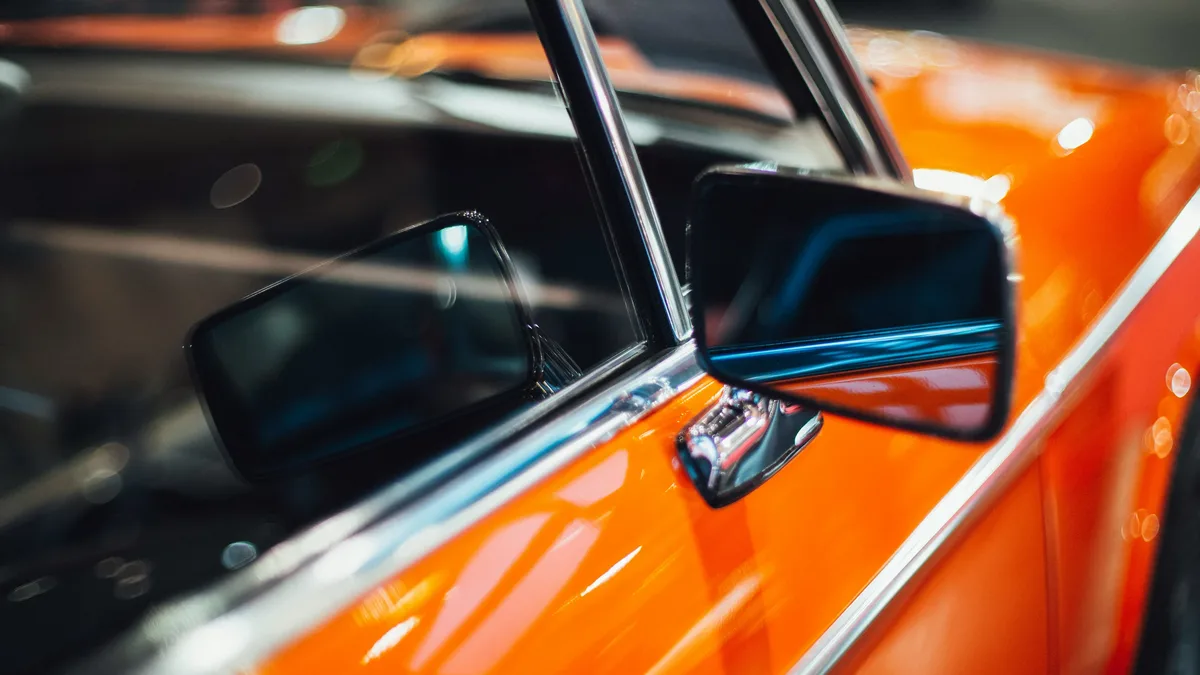 Auctions: The side of an orange car with a black side-view mirror and a window.