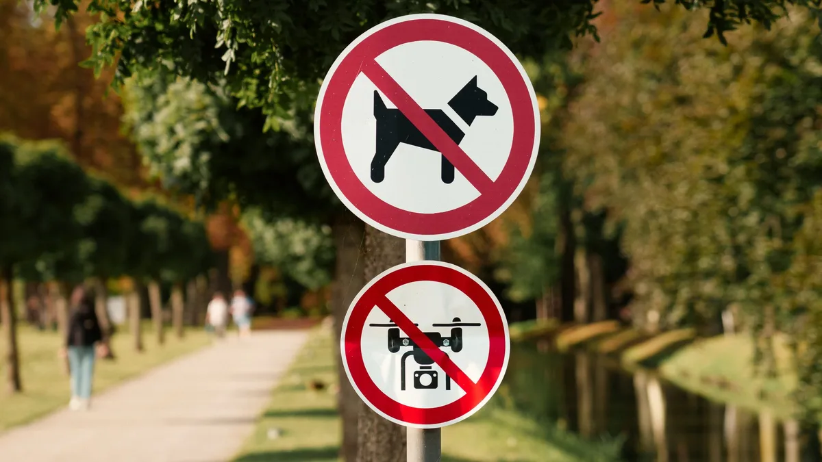 Two circular signs attached to a tree, with a red circle and line through a dog and a drone, indicating that dogs and