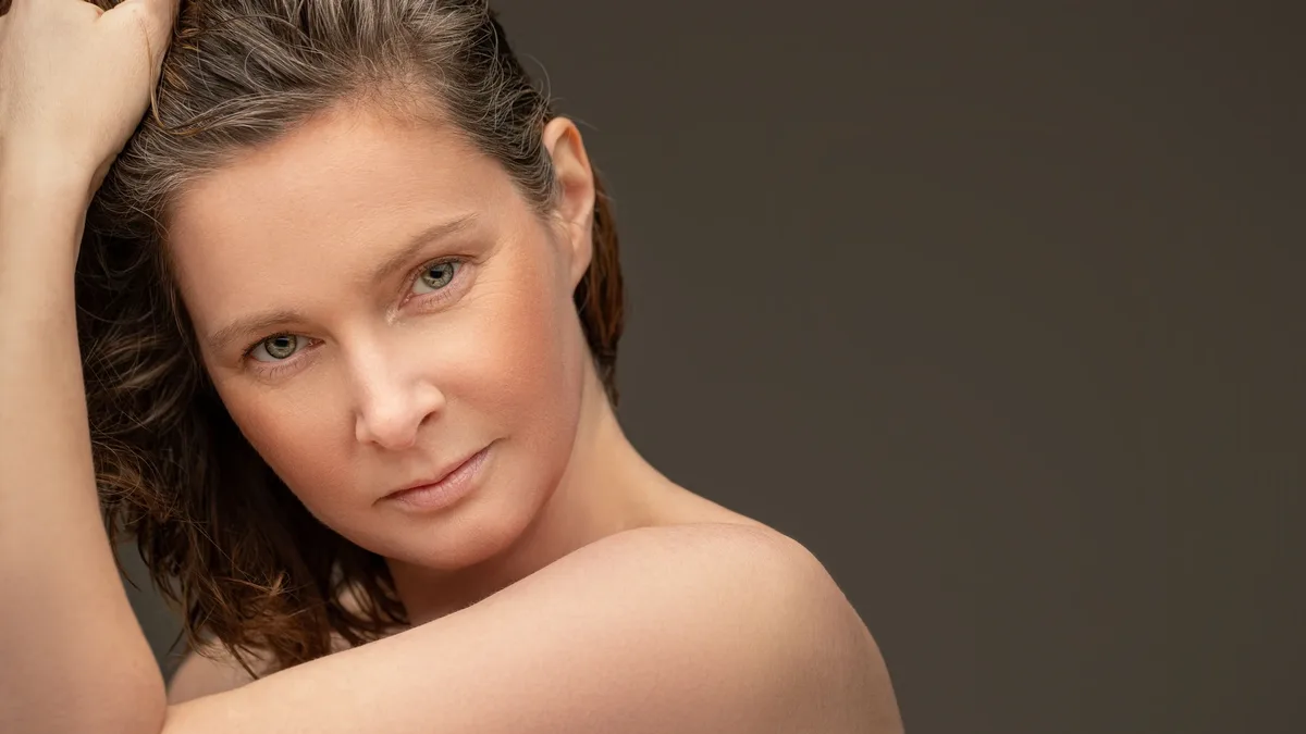 Care Systems: A woman with long brown hair, holding her hair up with her right hand, and looking directly at the camera.