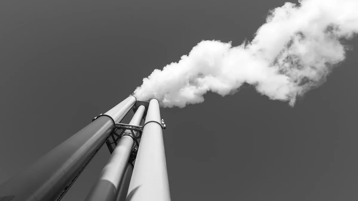 Impacts In Europe: Black and white image of a smokestack with smoke against a clear sky in Hamburg.