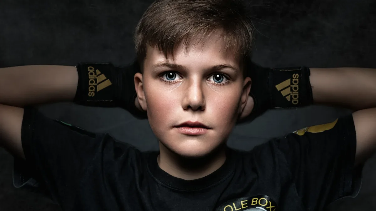 Levels: Close-up portrait of a young boy boxer wearing gloves with neutral background.