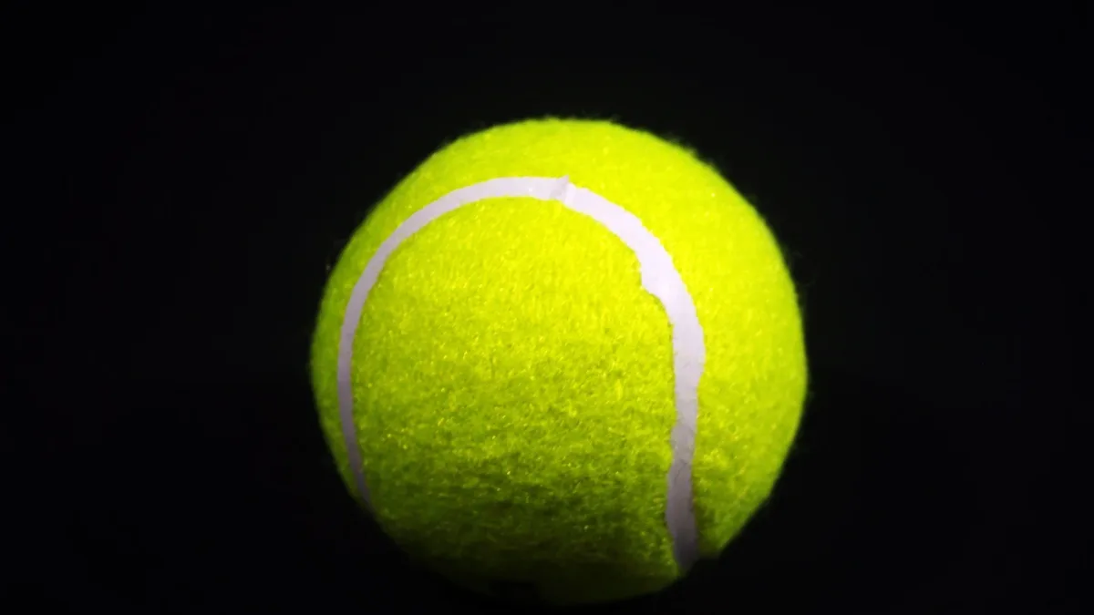 Players: Close-up of a bright yellow tennis ball against a dark background, highlighting texture and color contrast.
