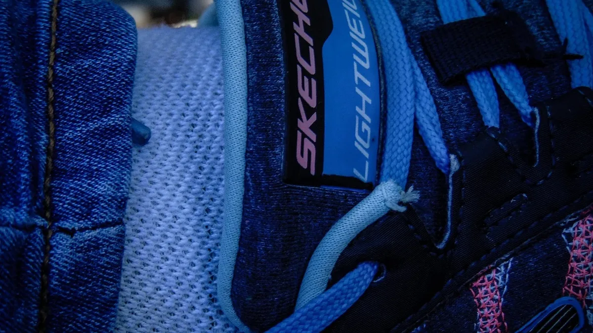 A close-up view of the side of a blue Skechers sneaker with a white shoelace and a black tag with the word "SKECHERS" in
