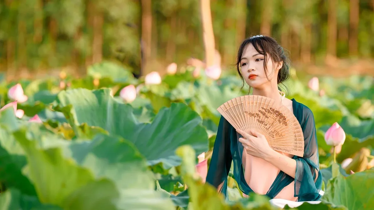 Tailoring: A woman stands in a field of lotus plants, holding a fan in front of her chest.