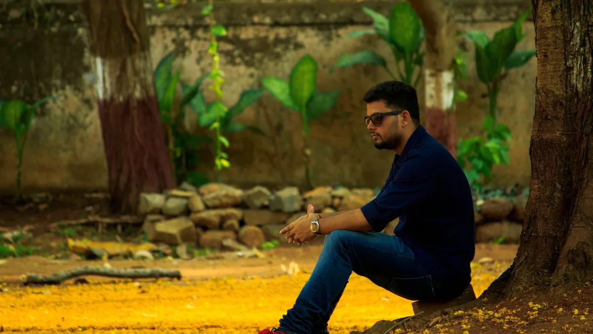 Career: A man sits under a tree in a sunlit park, enjoying a moment of leisure.