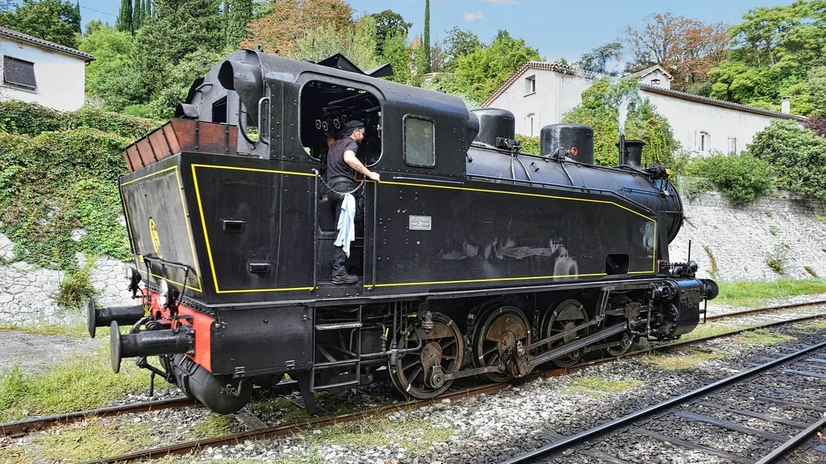 Stages: A black steam locomotive with a yellow stripe on the side, parked on a set of tracks in a residential area.