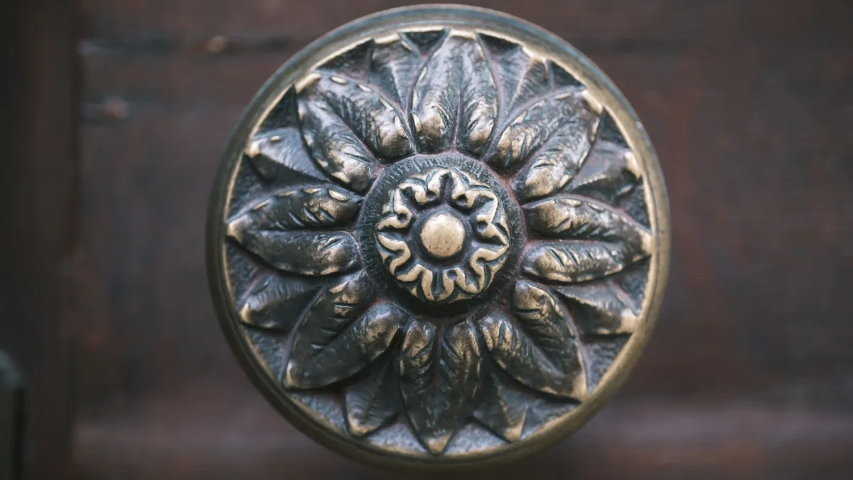 Pieces: Close-up of an antique metal door knob featuring an intricate leaf design in a floral pattern.