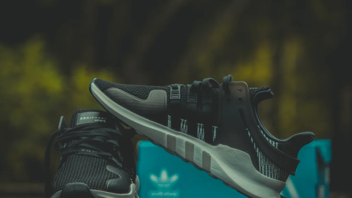 A pair of black and white Adidas sneakers with a teal box in the background.
