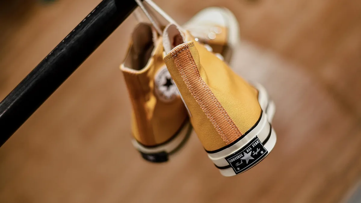 Yellow Converse sneakers with white laces hang from a rail.