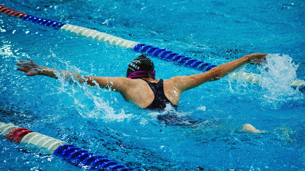Woman athlete doing butterfly stroke in pool during competition, vibrant and dynamic image. Swimming professional photography