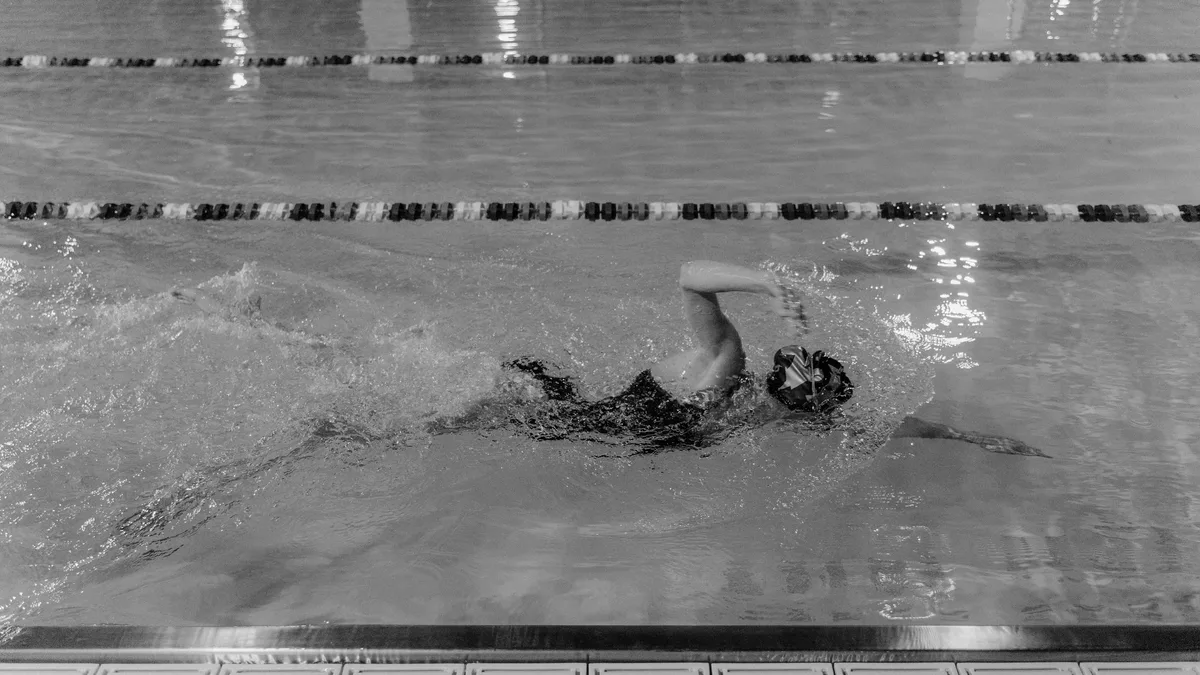 Competition: Focused athlete swimming in an indoor pool, captured in black and white.