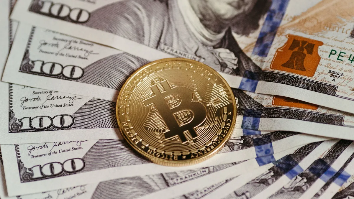 Labour Market: Gold Bitcoin coin resting on US dollar bills showcasing digital and traditional currency.