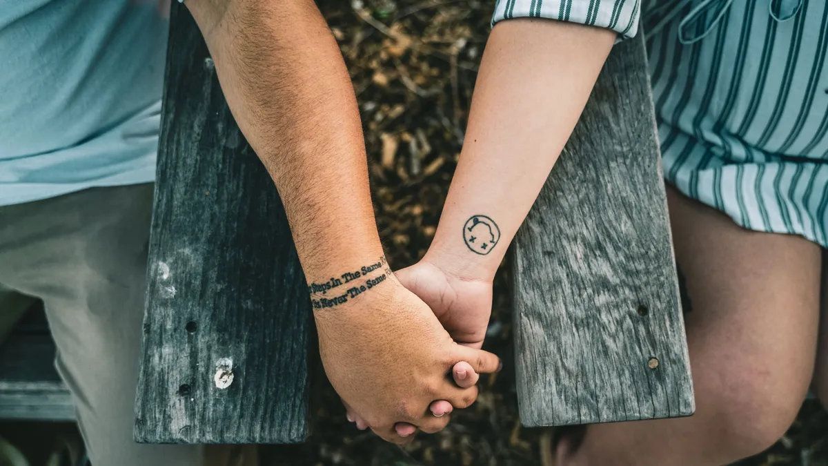 Endings: Intimate close-up of a couple holding hands with tattoos, symbolizing connection and relationship.