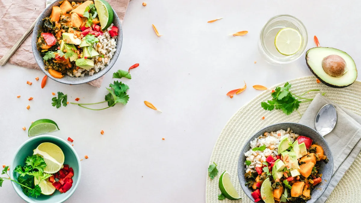 Ingredients: A table with two bowls of food, a glass of water, an avocado half, and a lime wedge.