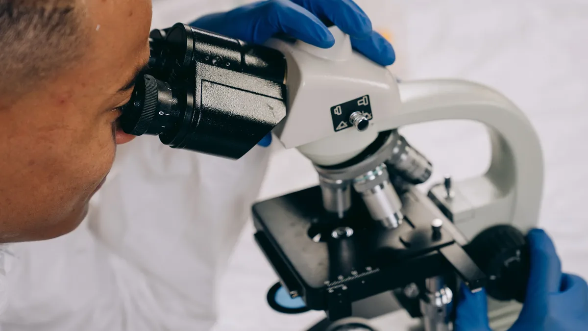 Ingredients: A person wearing blue gloves and looking through a microscope.
