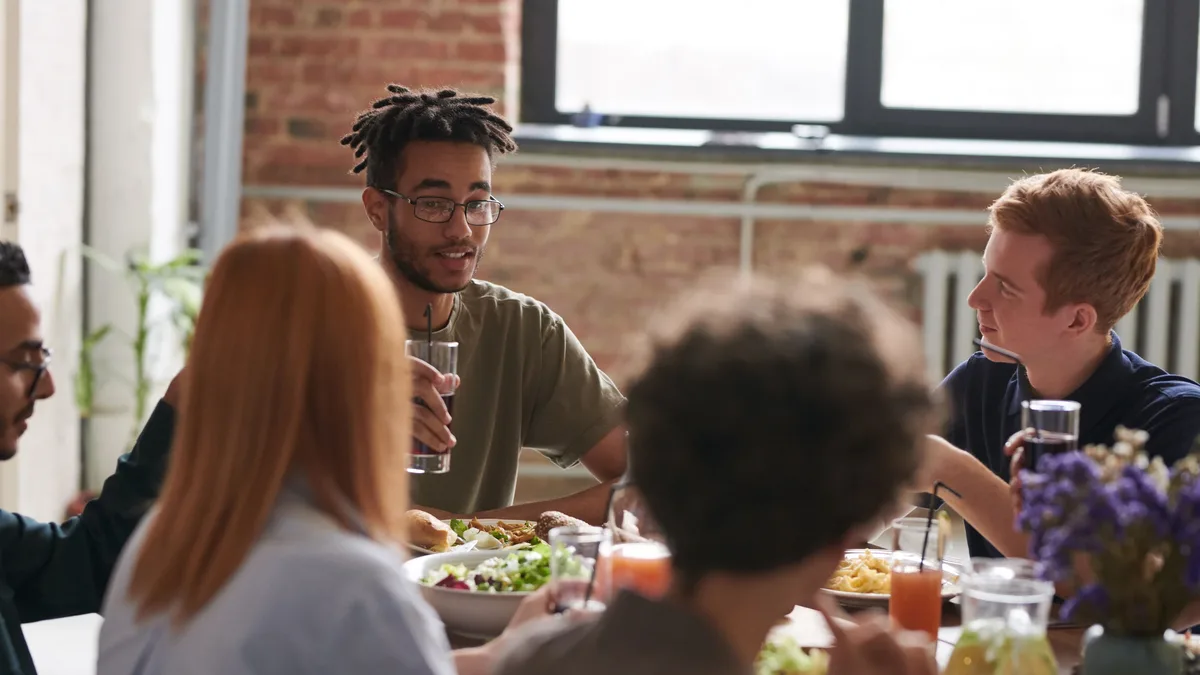 Five people are seated around a table, with four of them facing each other and engaged in conversation, while the fifth