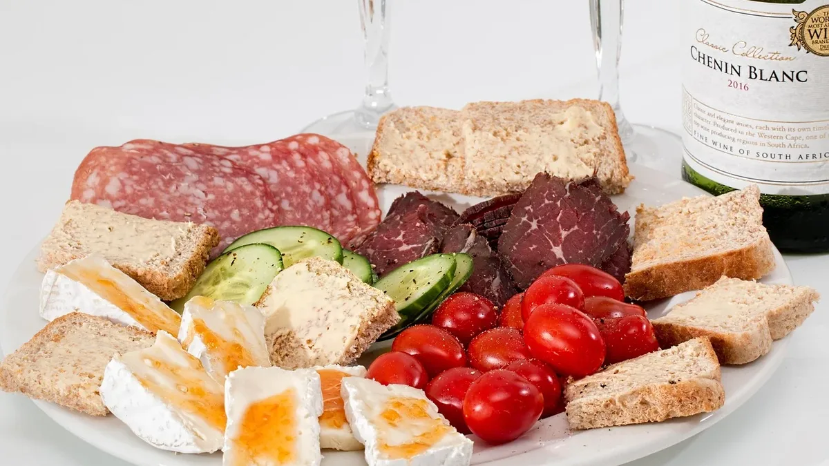 Culture: A plate of assorted cheeses, meats, breads, and vegetables, accompanied by a bottle of wine and a glass.