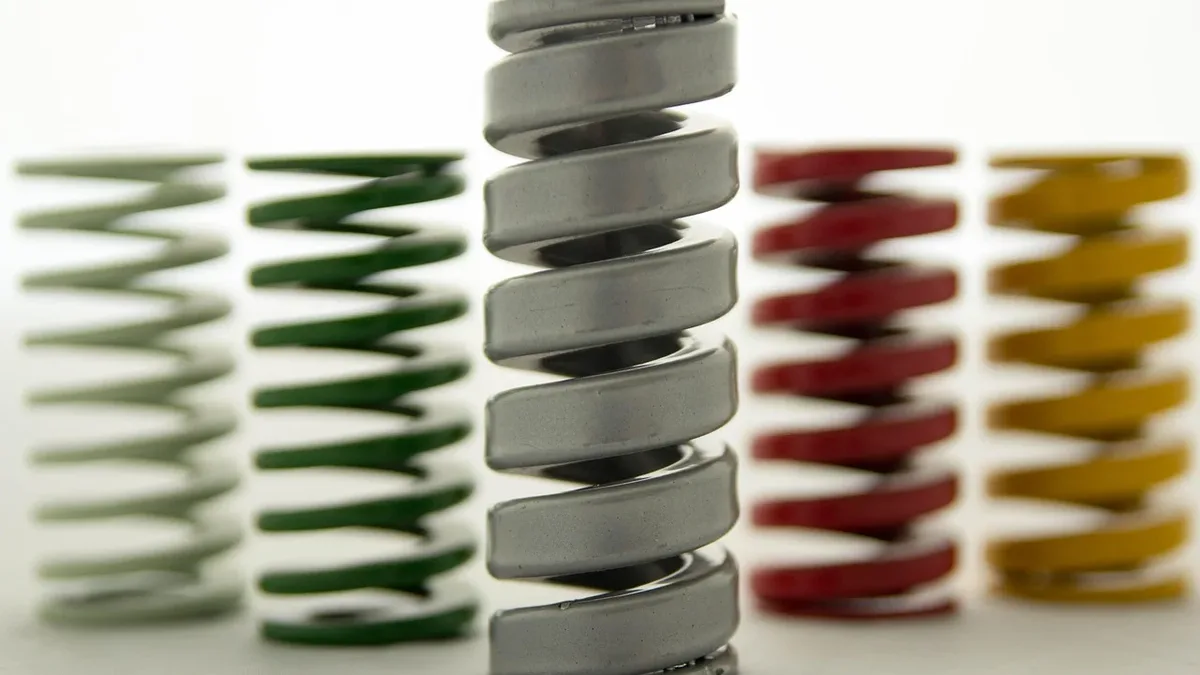 There are five metal springs of varying colors, including green, silver, red, and yellow, arranged in a row on a white