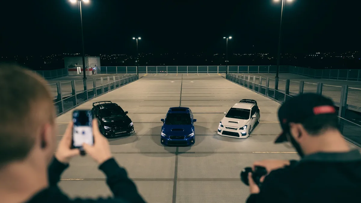 Reviews: Nighttime shot of three sports cars in a parking structure, with photographers capturing the moment.
