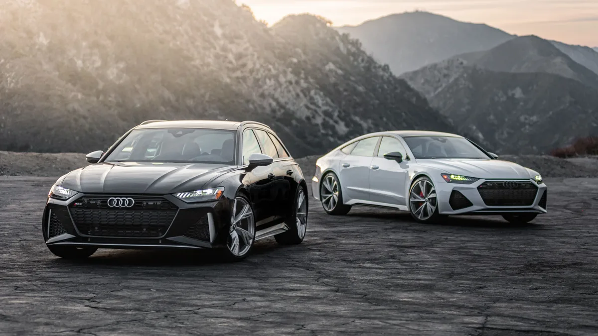 Compare: Two luxury Audi RS models parked on a scenic mountain road at sunset.