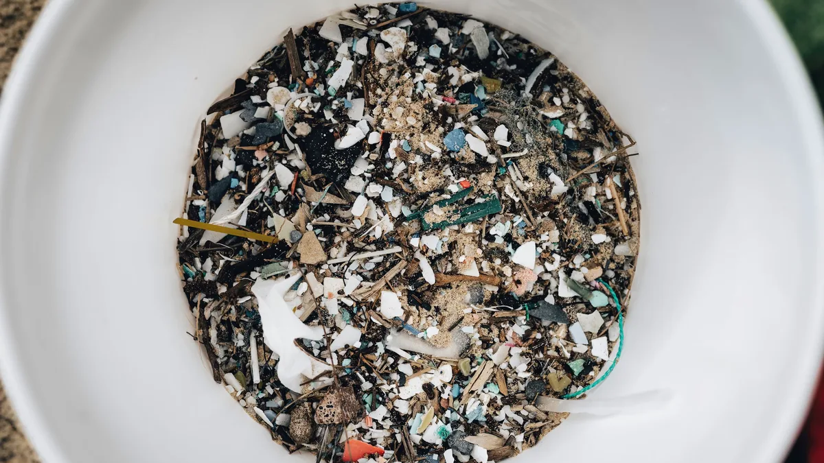 Water: Detailed view of microplastics and debris collected in a white circular container showing pollution.