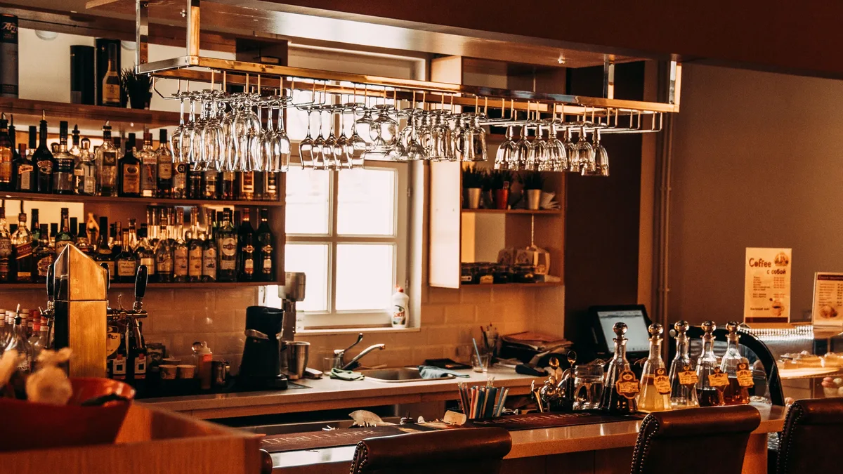 A stylish bar interior featuring hanging glassware, a range of spirits, and wooden furnishings. Restaurants & Dining industry