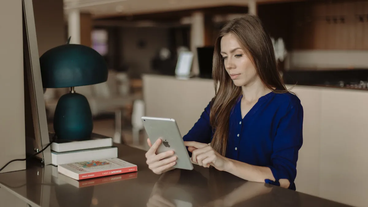 Authors Publishers: Woman reading on a tablet at a desk with books in a modern office setting.