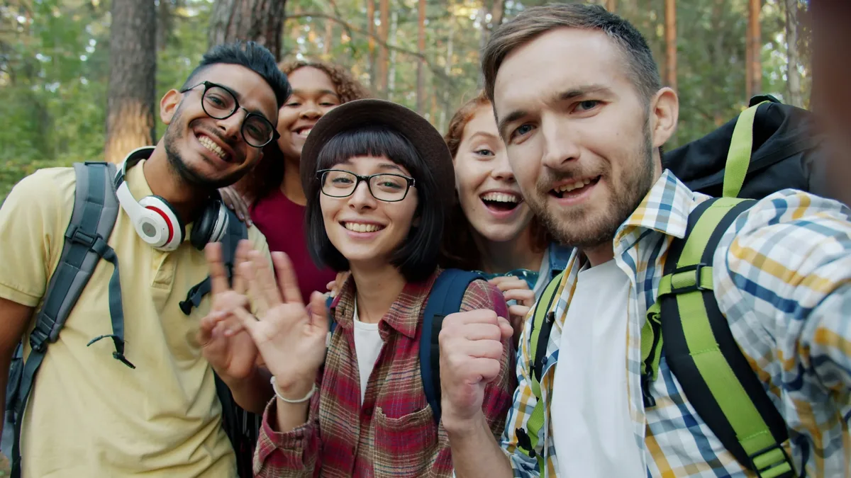 Point of view portrait of joyful young people friends taking selfie travelling in the forest together posing with funny