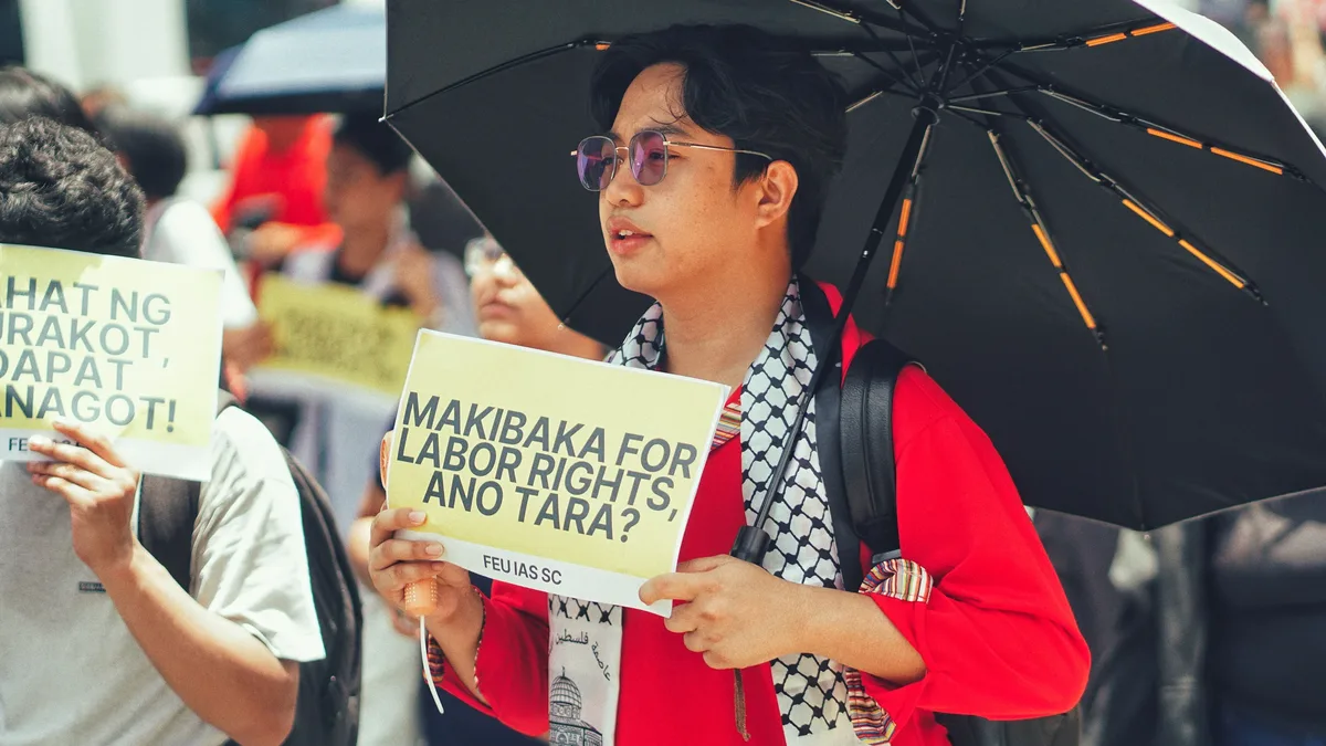Protest for labor rights featuring diverse participants holding placards and an umbrella for shade. Human Rights Politics